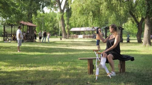 Une jeune fille avec un casting et des béquilles est assise dans le parc à regarder des amis s'amuser et jouer