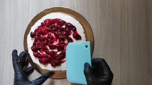 Gloved Hands Spreading Berry Sauce on White Cake