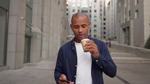 Man Using Phone Walking in City with Coffee