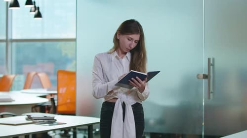 Busy Concentrated Caucasian Female Employee Standing in Office Analyzing Project and Looking at