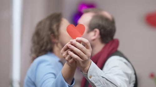 Romantic Couple Kissing Behind a Red Paper Heart