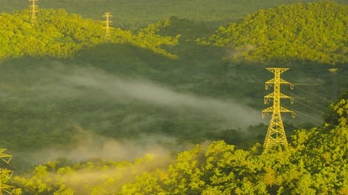 Aerial view high voltage power transmission towers or electricity pylon in fog on mountain.