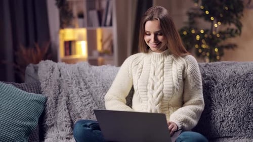 Smiling Woman Uses Laptop on Couch at Night