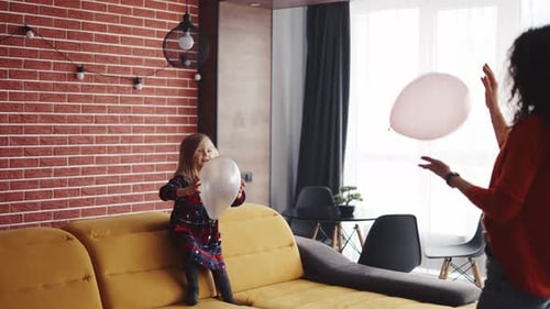 Girl and Woman Play With Balloons on Couch