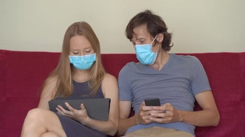 Couple Using Mobile Technology Wearing Medical Masks Indoors