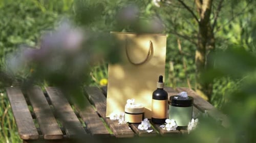 Cosmetic bottle and jar next to shopping bag on wooden table in blooming tree garden