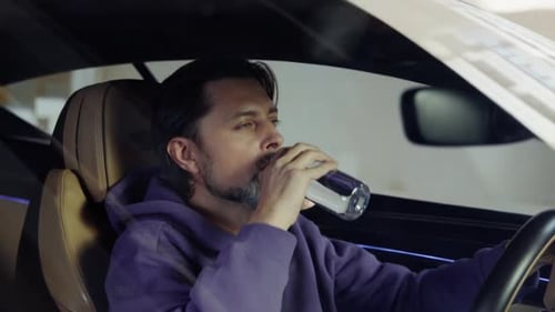 Man Driving Car in the City Drinking Water