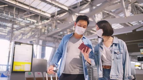 Asian Man and woman passengers wearing face mask walking in airport terminal to boarding gate.