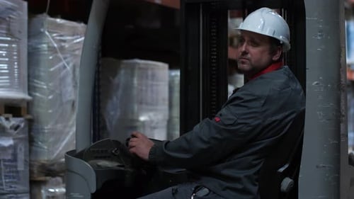 A Man in a Helmet Riding a Forklift Along the Warehouse