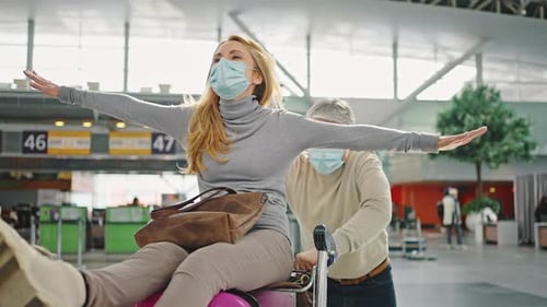 Woman Rides Luggage as Man Pushes at Airport