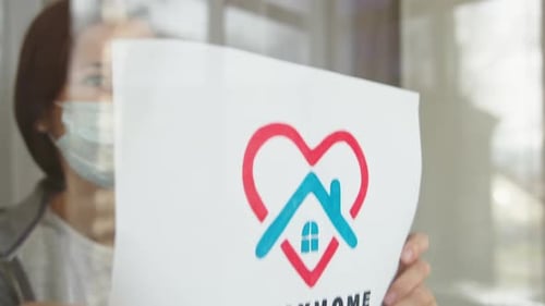 Woman Behind Glass Holds Stay Home Sign