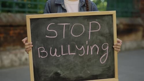 Little Girl Standing Demonstrating Alone Holding and Raising Schoolboard with Text Stop Bullying on