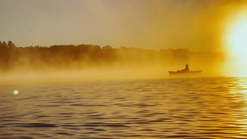 Kayaker Floats on Calm Water Through the Morning Fog Above the Water at Sunrise the Silhouette of a