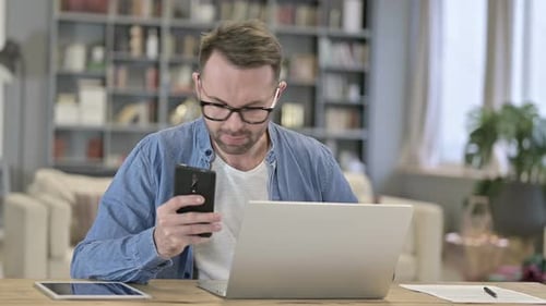 Man Using Smartphone with Laptop at Home Office