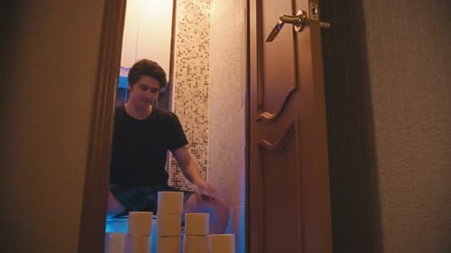 Ein junger Mann sitzt mit einem Haufen Toilettenpapier auf einer Toilette und schließt die Tür