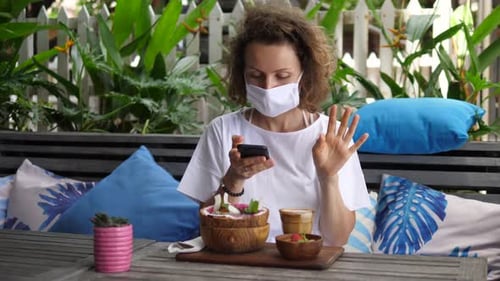Woman In Mask Using Phone At Tropical Cafe