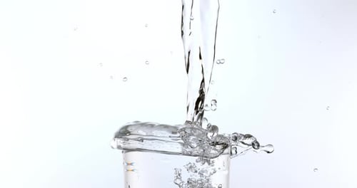 El agua se vierte en el vidrio sobre fondo blanco, cámara lenta 4K