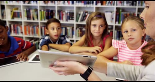 Teacher teaching school kids on digital tablet in library
