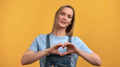 Woman Makes Heart Shape with Hands on Yellow Background