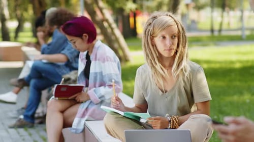 Female College Student Writing in Notepad Outdoors in Park