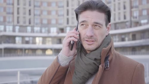 Portrait of Handsome Confident Man in Brown Coat Standing in the City Street Talking By Mobile Phone