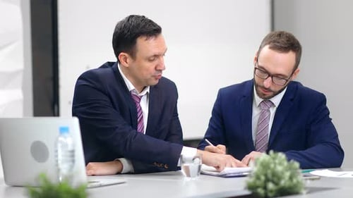Collaboration entre un homme concentré et un patron en costume avec un employé de sexe masculin qui rédige des notes sur le lieu de travail
