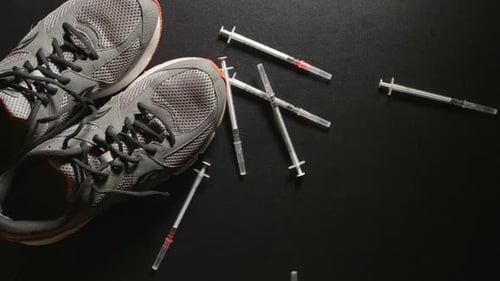 DOPING: Zeitlupenaufnahme von Spritzen, die in der Nähe eines Turnschu