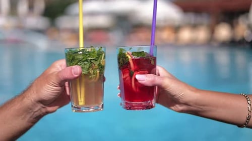 Gebräunte Hände klirrender Gläser, kalt, frisch, tropischer Cocktail, Stroh, Sonnenbaden in der Nähe des Pools