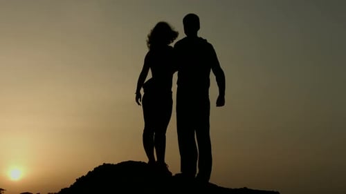 Silhouetted Couple Embracing atop Hill at Sunset