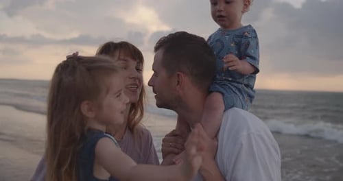 Young Parents Stand on the Sea Coast, Holding Their Little Children, Kissing