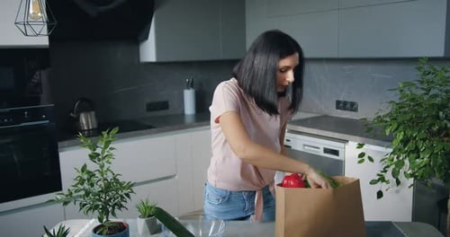 Brunette which Unpacking Food Bag and Putting Groceries on Kitchen Table