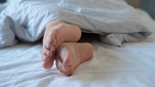 Female Legs in the Bed Under Blanket