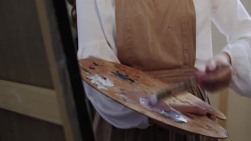 Joven artista mezclando colores en la paleta y aplicándolos en el lienzo