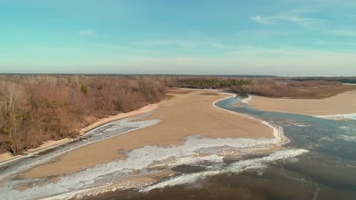 Drohnenaufnahmen aus der Luft vom Flug über ein sandiges Ufer mit einem kleinen Fluss im Winter