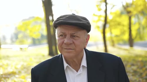 Portrait of a Pensive Senior Man in a Cap Looking at One Point in an Autumn Park