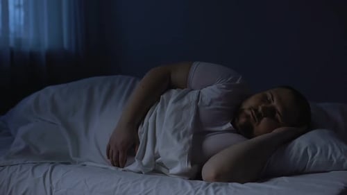 Homme obèse se jetant dans son lit la nuit, trouble du sommeil, insomnie, apnée