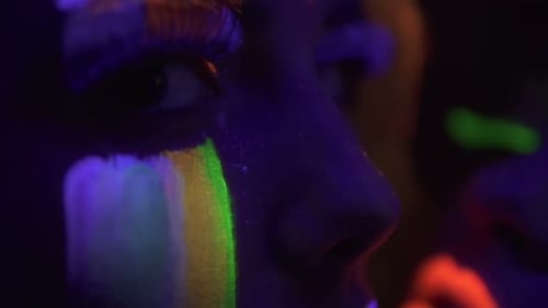 Closeup View of Two Beautiful Girls with Fluorescent Makeup Under UV Black Light Petting Each Other
