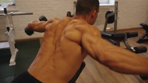 Bodybuilder im Fitnessstudio hebt Hantel an, während er auf einer Schrägbank liegt, mit dem Gesicht nach unten, um