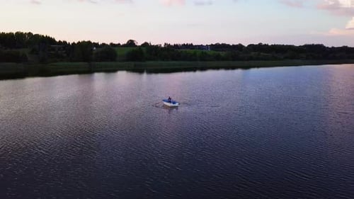 Friedlicher Sonnenuntergang an einem See. Mann auf einem Tretboot. Wunderschöne Farben. Drohnenschuss.