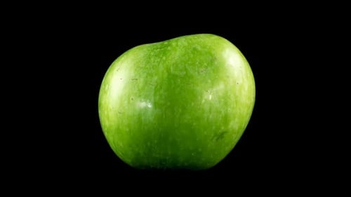 Rotating green apple against black background close up