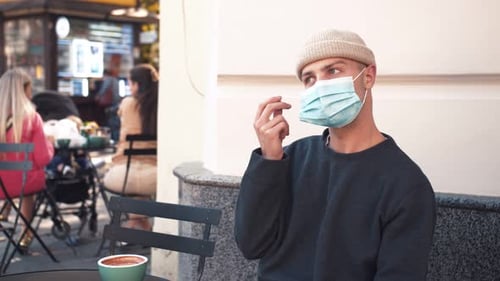 Close Up of Face of Young Handsome Caucasian Man Taking Off Medical Mask at Cafe. Looking Straight