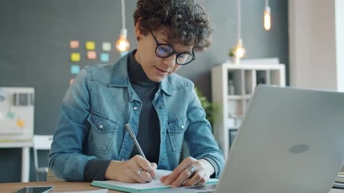 Attractive Girl Using Laptop and Taking Notes in Office Working Alone in Creative Workplace