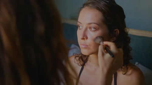 Woman Applying Makeup with Brush in Bedroom