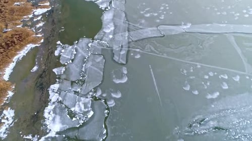 Aerial view of ice on the edge of a lake with cracks in the surface