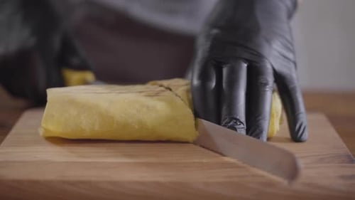 Gloved Hands Cutting Delicious Wrap on Wooden Board