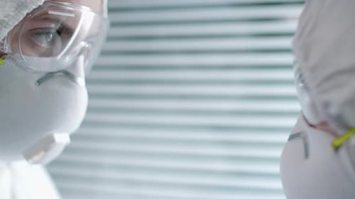 Two Hospital Workers in Protective Suits and Masks Talking at Work