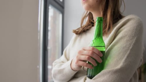 Young Woman Drinks from Green Bottle Indoors