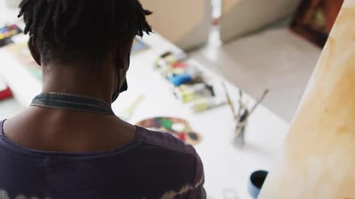Rear view of african american male artist mixing colors in the palette with a brush at art studio