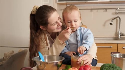 Smiling Woman Feeding Baby in a Kitchen