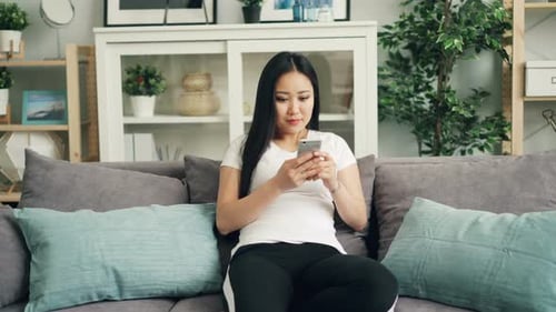 Woman Relaxing on Sofa Using Smartphone